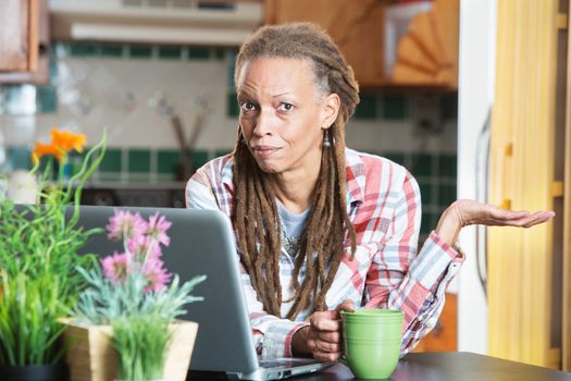 Single unimpressed woman in kitchen with computer and coffee with palm up