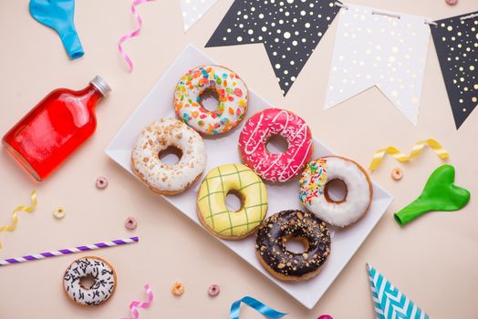 Party. Different colourful sugary round glazed donuts and bottles of drinks on light color background.