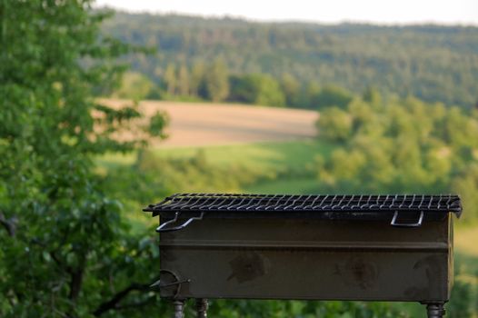 a empty portable BBQ grill in front of a fresh green summer landscape