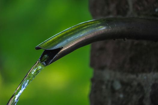 Close up of running water from a tap on brick wall on green background