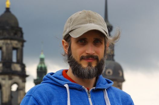 a young bearded man standing in front of a church on the background gun on abandoned building background