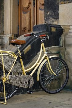 an old yellow bicycle. leather seat with shock absorbers and wheel in front of a church