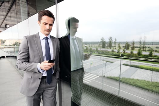 Handsome business man using a cell phone outdoors on the balcone of office building