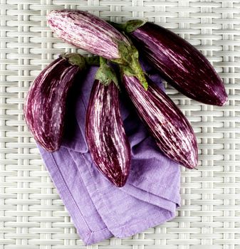 Stack of Fresh Raw Striped Eggplants on Purple Napkin closeup on Wicker background