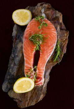 Raw Salmon Steak with Slices of Lemon and Rosemary on Shale Stone Board closeup on Dark Wooden background. Top View