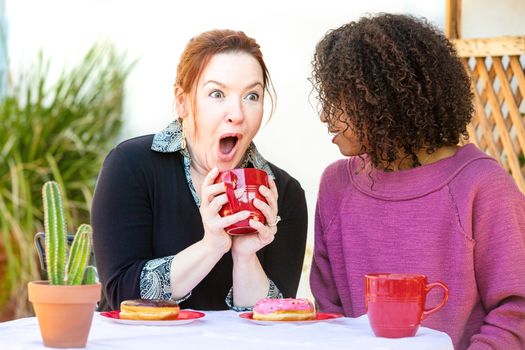 Happy female couple seated outdoors at restaurant sharing secrets