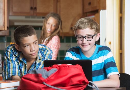 Smiling mother watching son and friend do homework at kitchen table