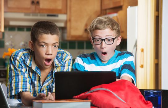 Surprised teen students looking at laptop computer at home in kitchen