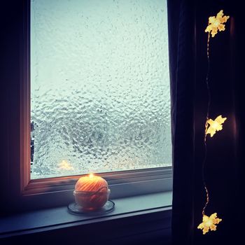 Cozy winter composition with frosted window, candle, and lights. 