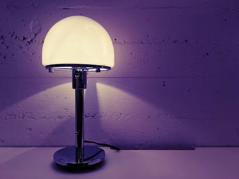 Contemporary design table lamp near concrete wall. Purple shades.