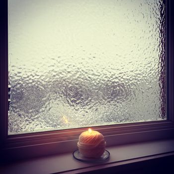 Frosted winter window and burning candle. Murky winter light.