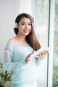 Asian woman enjoying view on windowsill and listening to music.