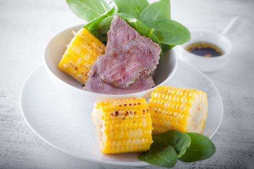 Beef and grilled corn served on a white plate