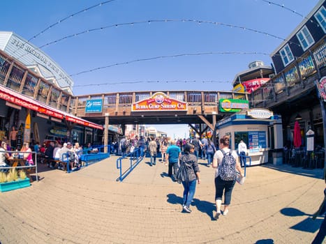 San Francisco, CA, USA - April 3, 2017: Tourists walking near the entrance of Pier 39, Fisherman's Wharf, bridge with Bubba Gump Shrimp Co. sign above