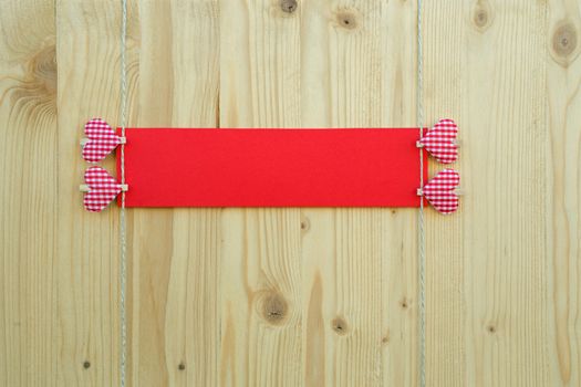 Two hearts with clothes pegs and red paper on a cord on wood