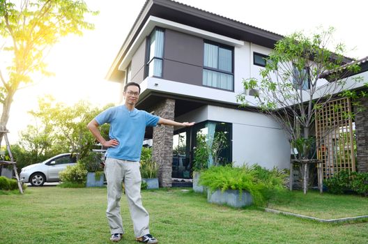 Man shows his new sian house , smiling and looking at camera, golden sunlight at background.