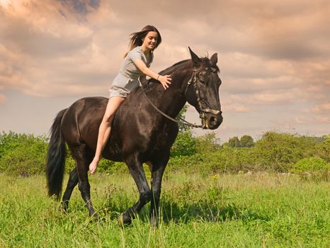 young riding girl and her black stallion in nature