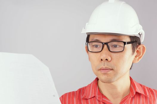 Engineer wear red shirt and white engineer hat with black spectacles is looking at document on white background.