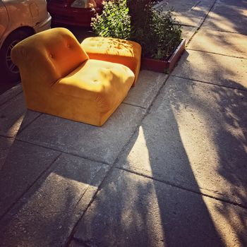 Abandoned orange sofa on the street, in sunlight.