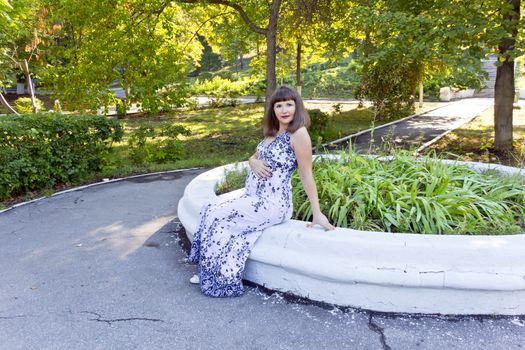 Pregnant woman with brown hair sitting in summer