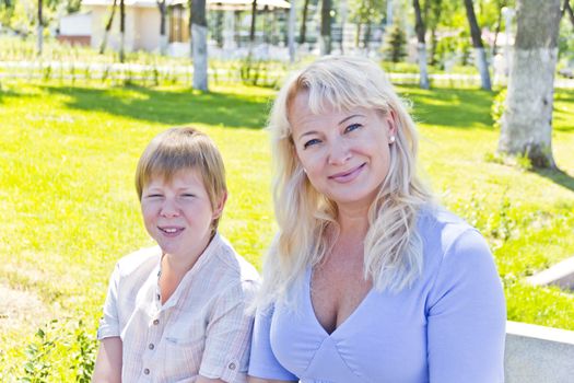 Happy blond woman and son smiling in the summer park