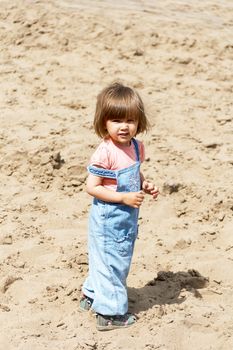 Cute Caucasian girl with short hair on sand background