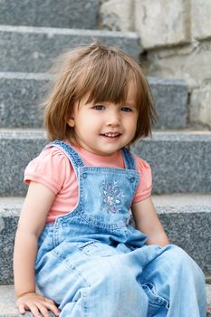 Baby girl in blue cloth sitting on the stone stairs