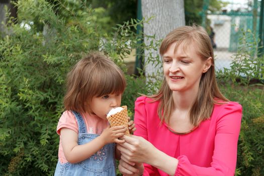 Mother and daughter in summer park are eating icecream