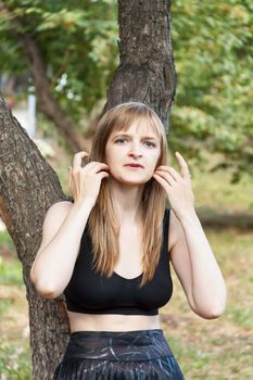 Beautiful blond woman corrects hair near tree in summer