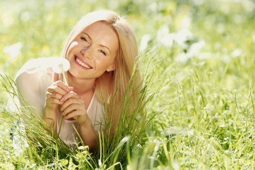 girl with a dandelion in his hand lying on the grass