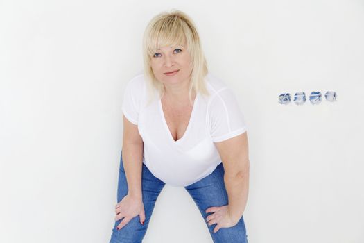 Blond woman in white and blue jeans inside empty room with opened wall plugs