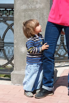 Cute Caucasian girl embrace mother leg in summer