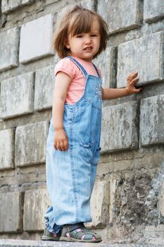 Baby girl in blue cloth standing near stone wall