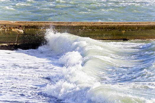 Sea waves with foam are breaking on the breakwater