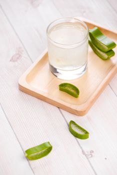 Glass of aloe vera juice with fresh leaves on a wooden table
