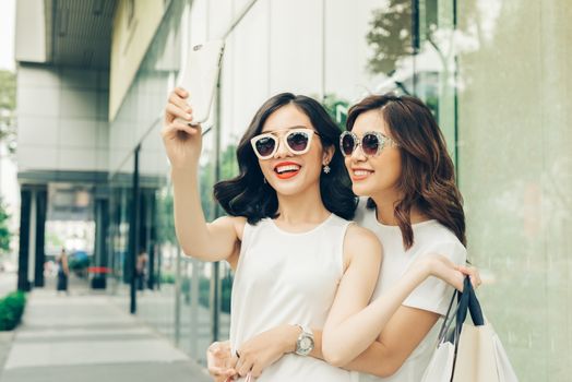 Beautiful asian girls with shopping bags taking selfie photo at the mall