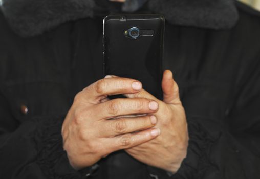 a man in a black jacket holding the phone in front of the two arms.