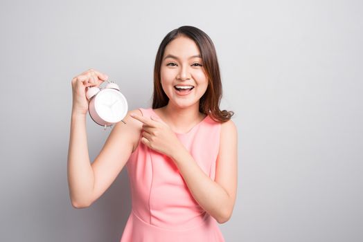 Pretty asian girl with surprised face holding an alarm clock in her hand and looking at it with opened mouth 