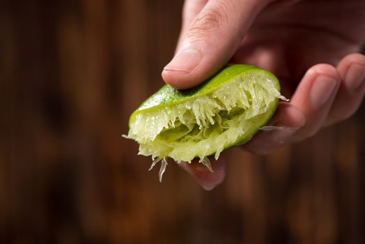 Hand squeeze lime with lime drop on dark wooden background