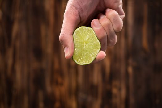 Hand squeeze lime with lime drop on dark wooden background