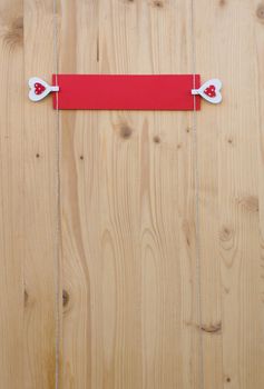 Two hearts with clothes pegs and red paper on a cord on wood