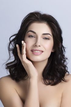 Portrait of a beautiful woman with perfect skin and dark curly hair touching face, skincare concept