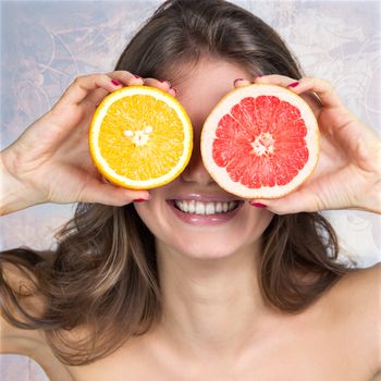 Smiling woman holding slices of orange and grapefruit in front of her eyes