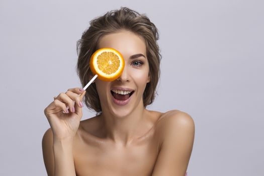 Young smiling woman cover eye with slice of orange