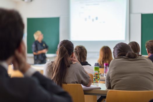 Teacher at university in front of a whiteboard screen. Students listening to lecture and making notes.