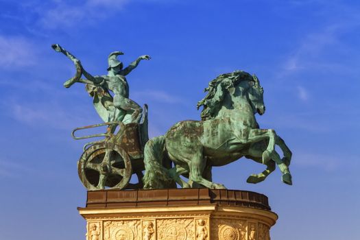 Statue representing War, a man holding a snake on a chariot, on a colonnade in Heroes Square or Hosok Tere by day, Budapest, Hungary.