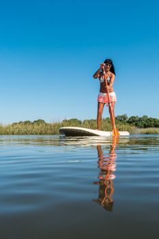 Woman stand up paddleboarding on lake. Young girl doing watersport on lake. Female tourist in swimwear during summer vacation.