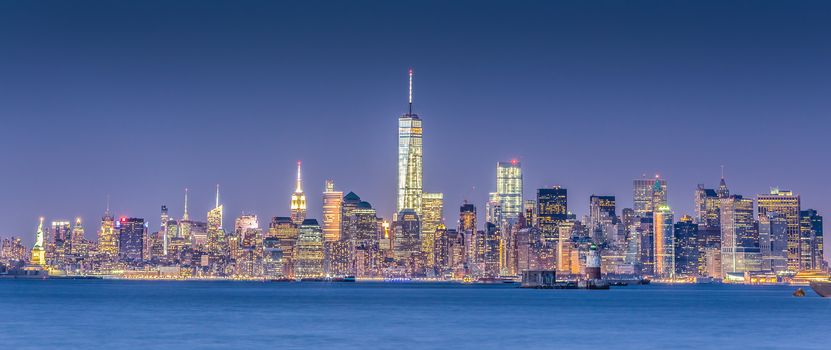 New York City Manhattan downtown skyline at dusk with skyscrapers illuminated over Hudson River panorama. Horizontal composition.