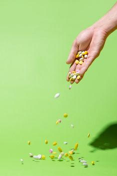 Colored pills falling from hand on green background.