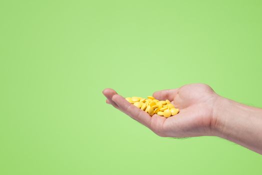 Yellow pills in hand on green background.